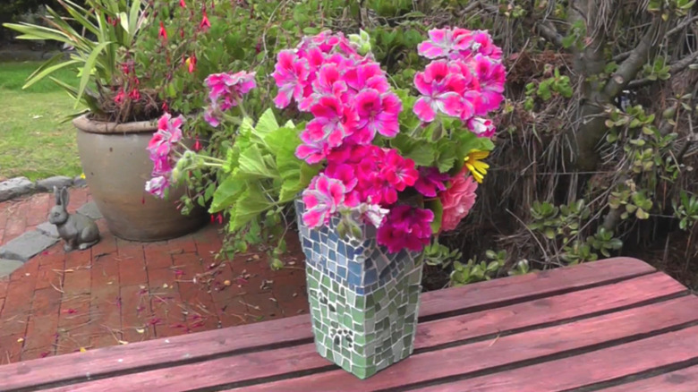 Squared vase covered with colorful glass pieces in a mosaic style with pink flowers in the vase