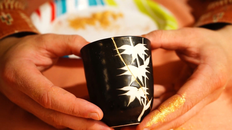 Person holding a ceramic container repaired with the Kintsugi method with the gold crack being visible