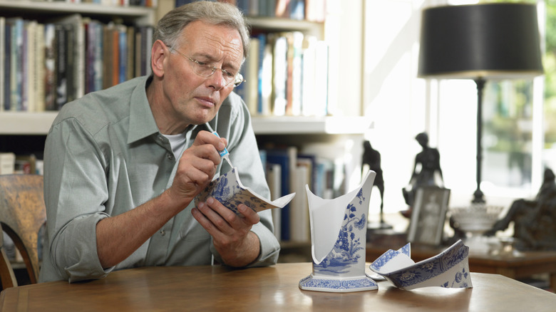 Man in a living room fixing a broken china vase