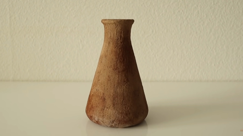 Repaired vase covered with textured paint sitting on a table next to other decor