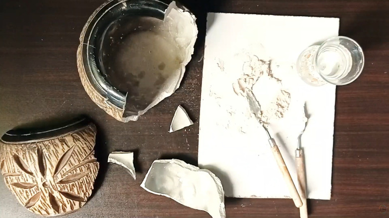 Person gluing the pieces of a ceramic vase together and the repaired vase on the left