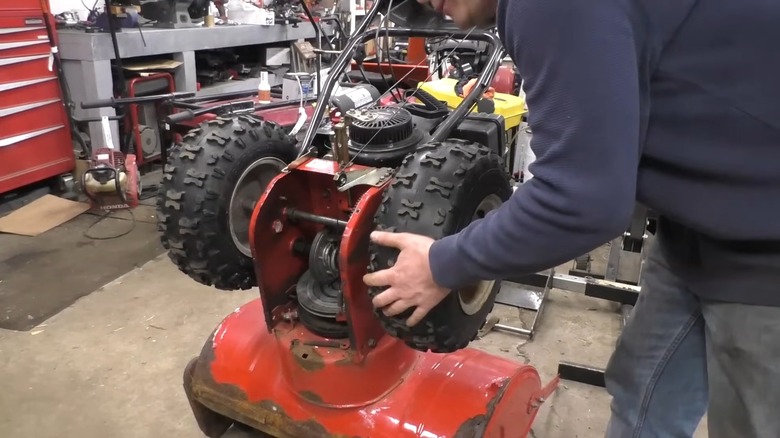 Man repairing a snow blower's wheels in his toolshed