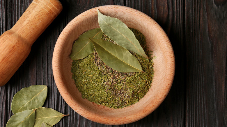 Bay leaves crushed into powder inside a mortar with a pestle nearby on the table