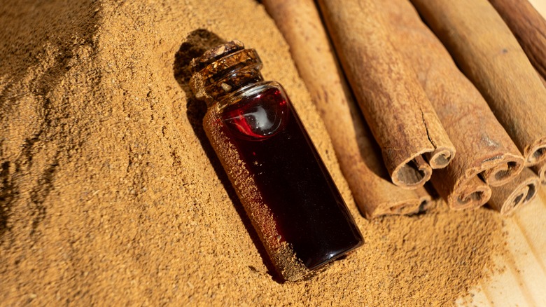 A vial of cinnamon oil with some cinnamon sticks on a pile of ground cinnamon