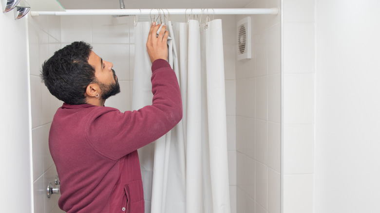 man hanging plain white shower curtain