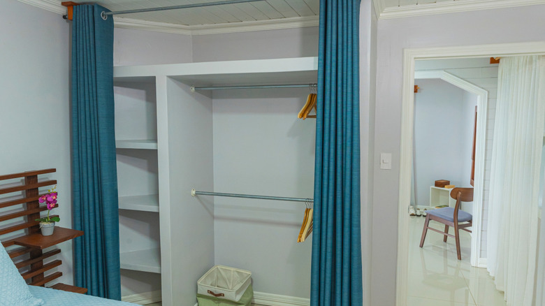 An opened blue curtain in front of an empty closet.