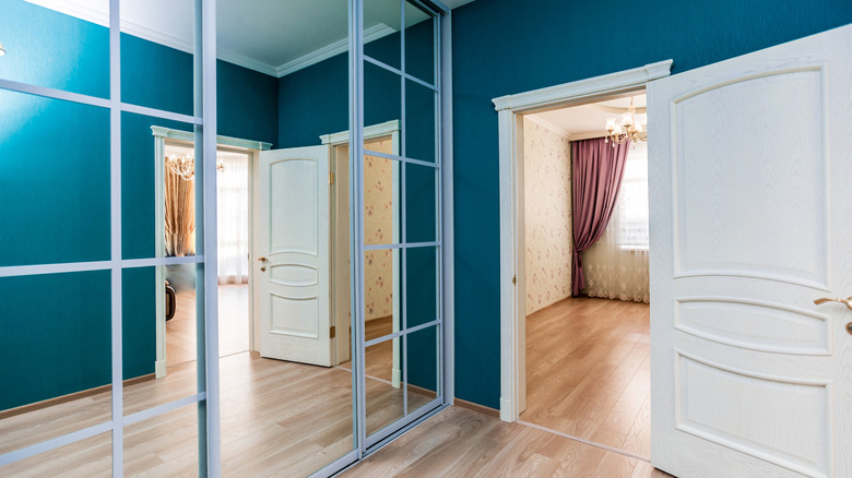 A closet with a mirrored door next to an open door.