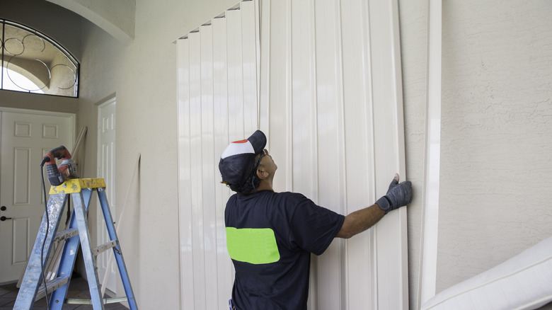 A contractor installs a white accordion door over a large storage closet in the entryway of a new-build home.