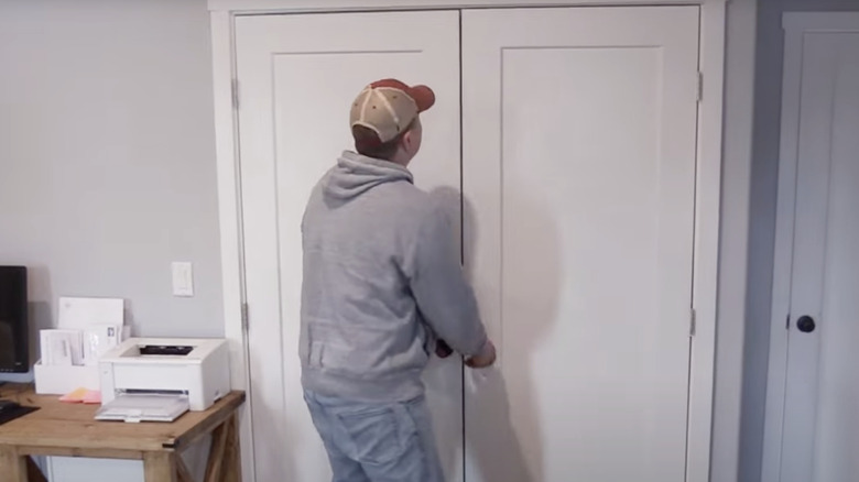 A man closes the French doors on a closet in an office.