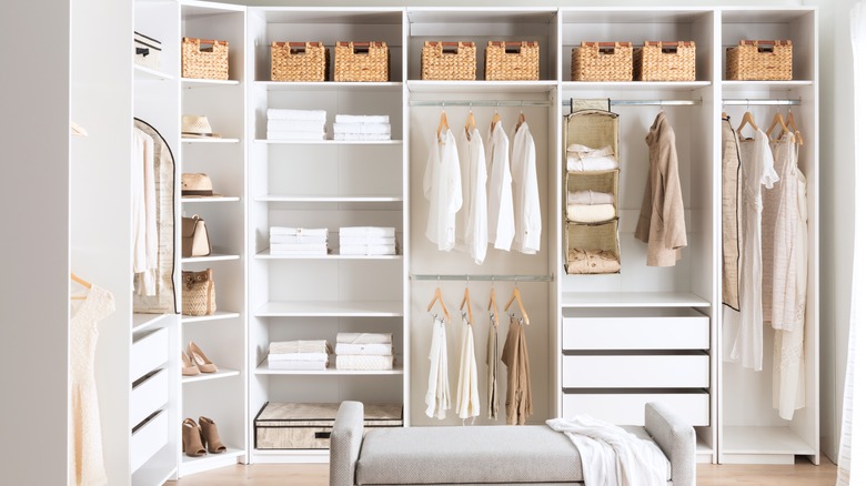 A white open closet with bins and clothing.