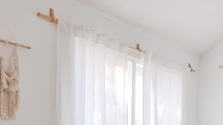 Leather curtain rod holders holding up white curtains in a bright bedroom