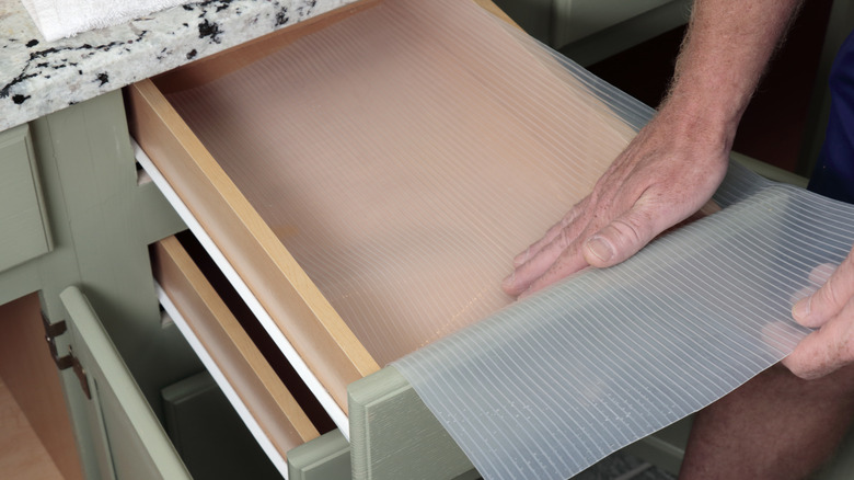 A person lining drawers with a plastic liner.