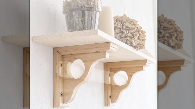 Two wood corbels with a shelf on top holding decorative flowers and a candle