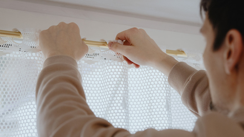 A person hanging a lace window valence