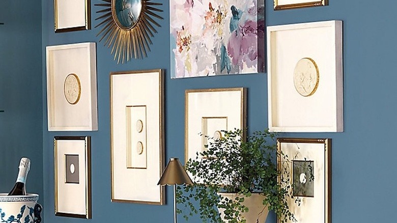 A blue wall hung with a gallery of art, intaglios, and a mirror.