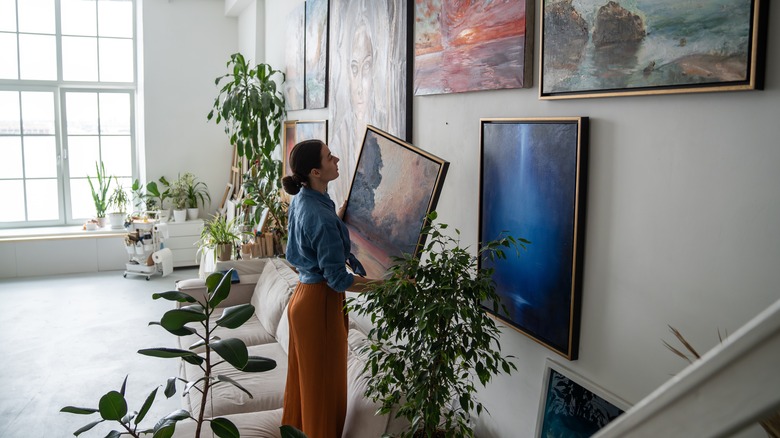 A woman removes the art from a gallery wall in a spacious living room.