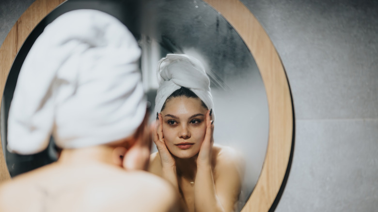 Woman in a bath towel looking at her reflection in a foggy mirror.