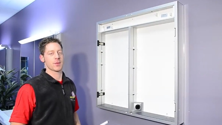 A man works on installing a medicine cabinet.