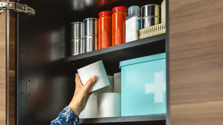 A woman's hand placing toilet paper in medicine cabinet