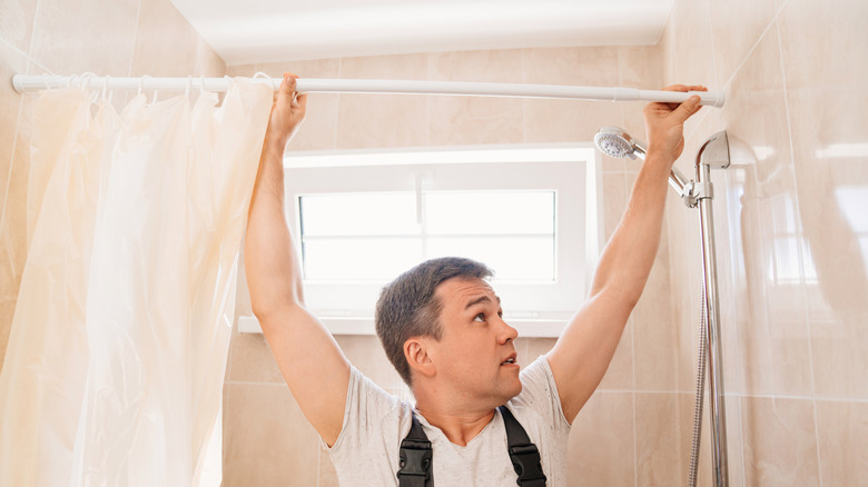 A person removes a shower curtain and curtain rod from a tiled shower