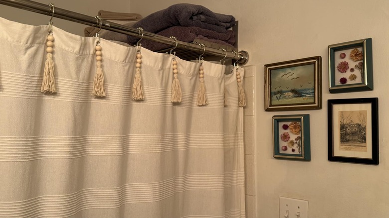 A beige shower curtain hung on boho hooks with tassels and wood beads