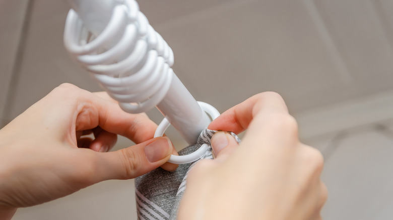 Hands hanging a shower curtain on white plastic hooks