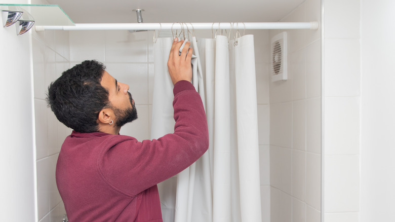 a man replacing the shower curtain hooks in their bathroom