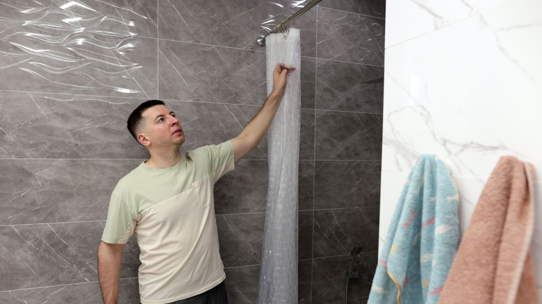 A person hanging a shower curtain in a bathroom