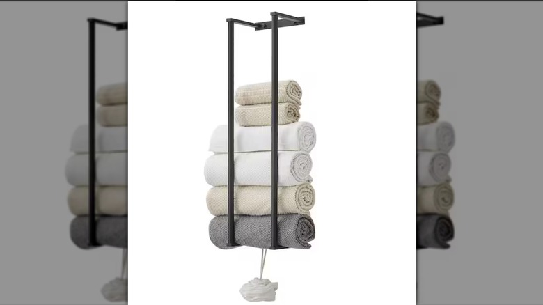 A wall-mounted towel rack with two vertical braces holding towels and a body puff hanging from the base.