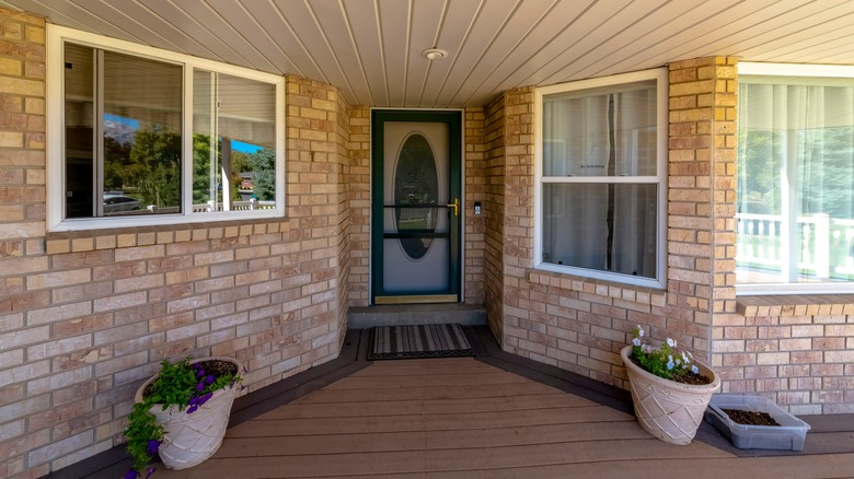 A green and white front door with oval glass surrounded by brick facade