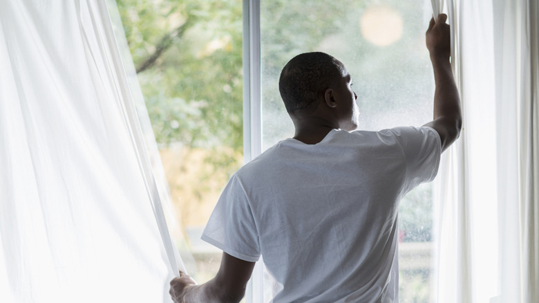 Man moving curtain on screen door