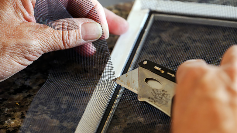 Person trimming excess window screen from window frame