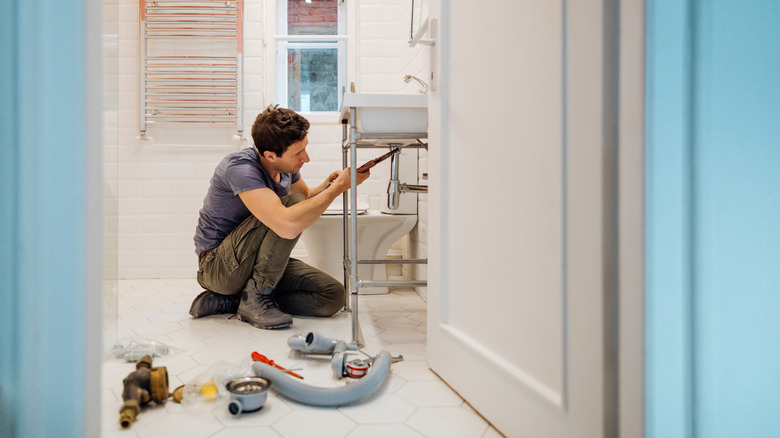 A man repairing an old-fashioned sink in a bathroom