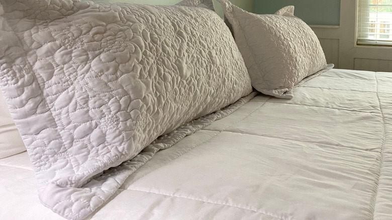 White pillow shams on a bed, with mint green walls in background.