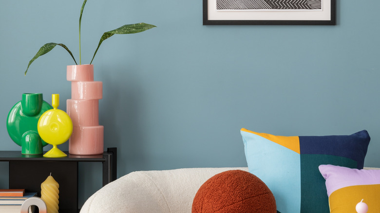 Blue wall behind sofa and side table with colorful ceramic decor.