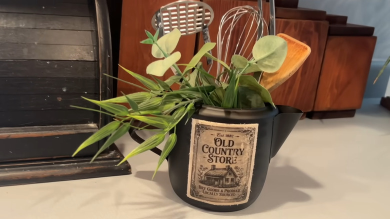 black upcycled teapot as utensil holder with an "old country store" decal on the front