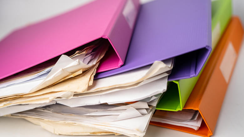 A stack of colorful three ring binders overflow with papers.