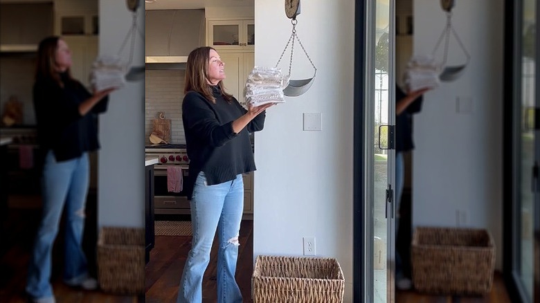 A person putting kitchen towels in a vintage hanging scale with a dirty linen basket underneath