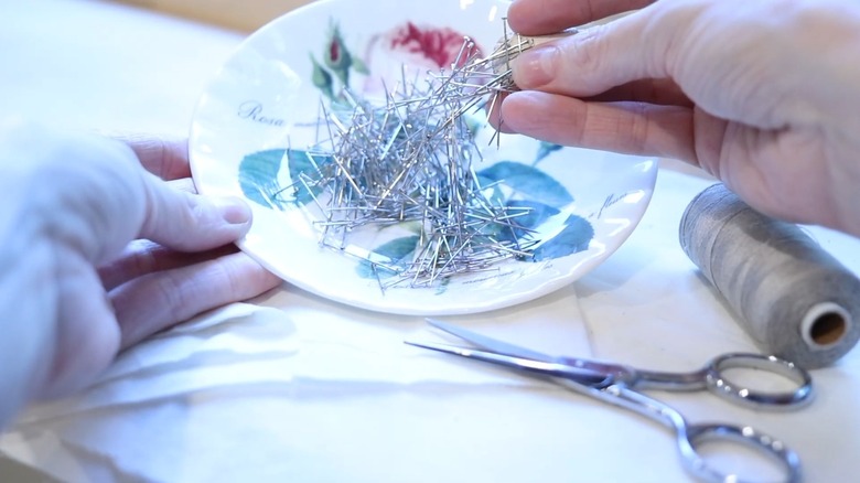Person picking up pile of needles on magnetic pin cushion plate