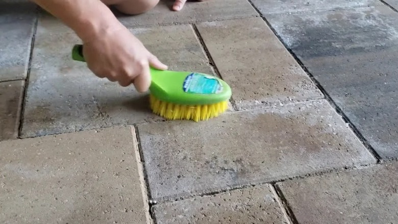 Scrub brush being used to clean pavers
