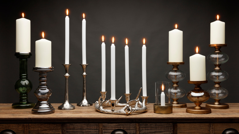 A collection of candle holders and candle sticks in metal and glass.