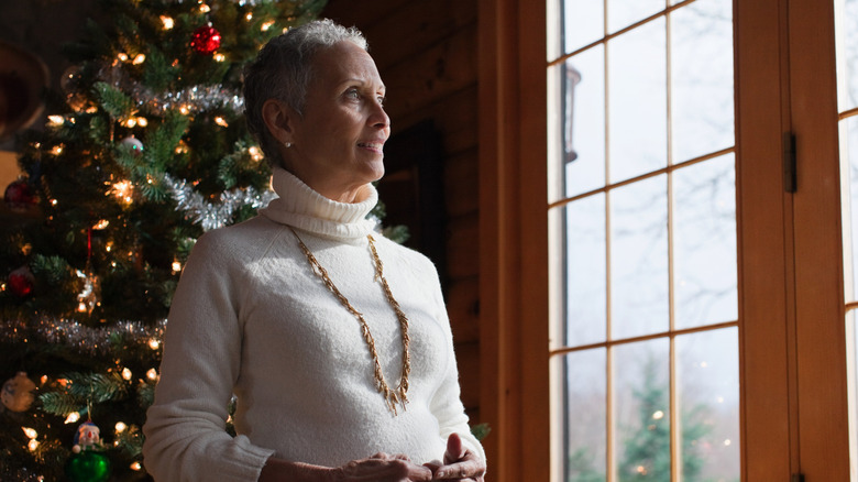 Woman looking out window with Christmas tree in background