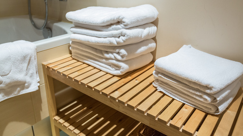 White bath towels folded and stacked on a two-tiered wooden storage piece
