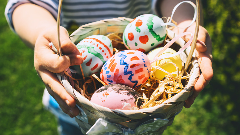 An Easter basket with colored eggs being held by a child