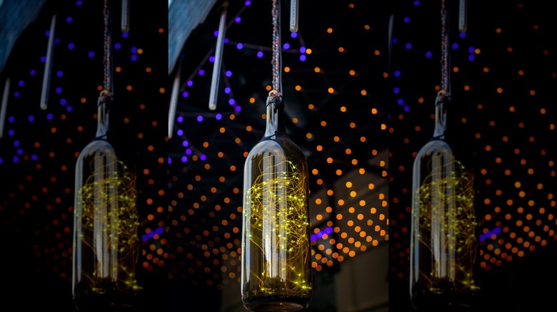 A wine bottle filled with lit fairy lights hangs from a pergola in the evening