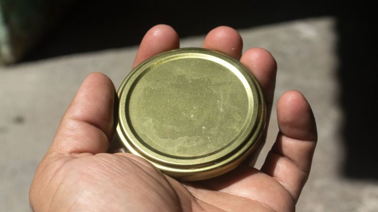 A man's hand holds a gold canning lid for a jar