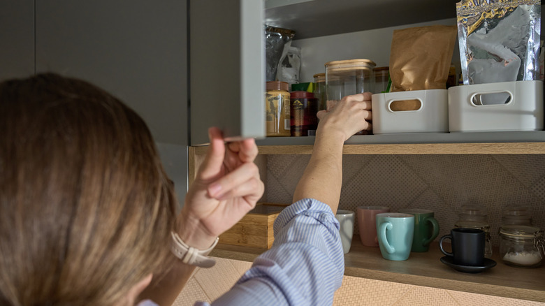 Woman reaching for a jar in an organized kitchen cabinet
