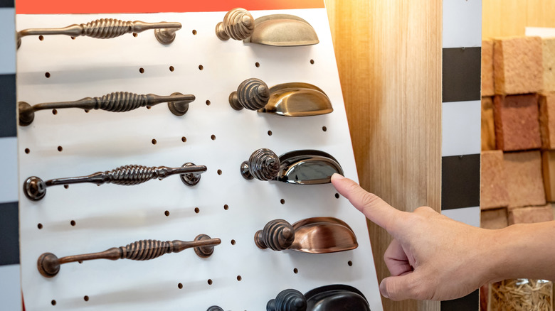A hand points at metal cabinet pulls on display in a home renovation store.
