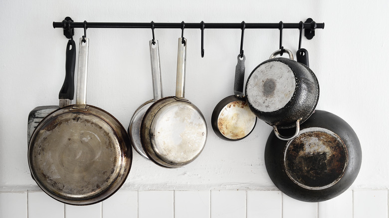 Old cooking pots hang on a wall rack in a kitchen.