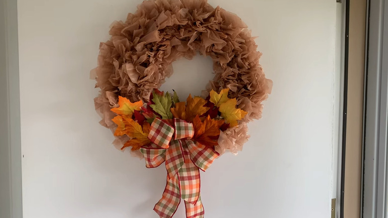 Wreath made of brown plastic trash bags and affixed with decorative leaves plus a plaid bow